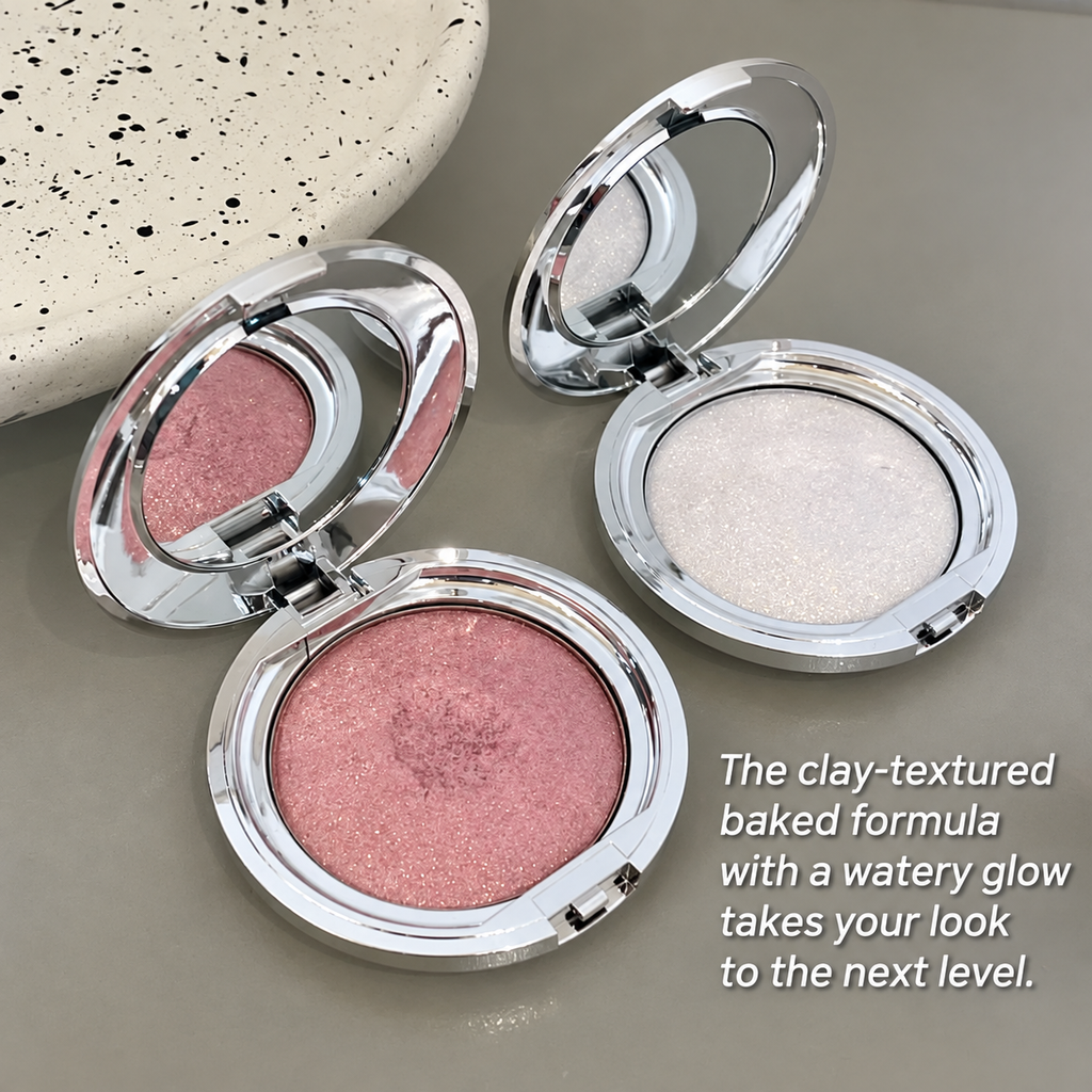 Two round open makeup compacts with mirrored lids on a neutral gray surface. One compact contains a shimmery pink pressed powder, and the other contains a bright shimmery white powder.